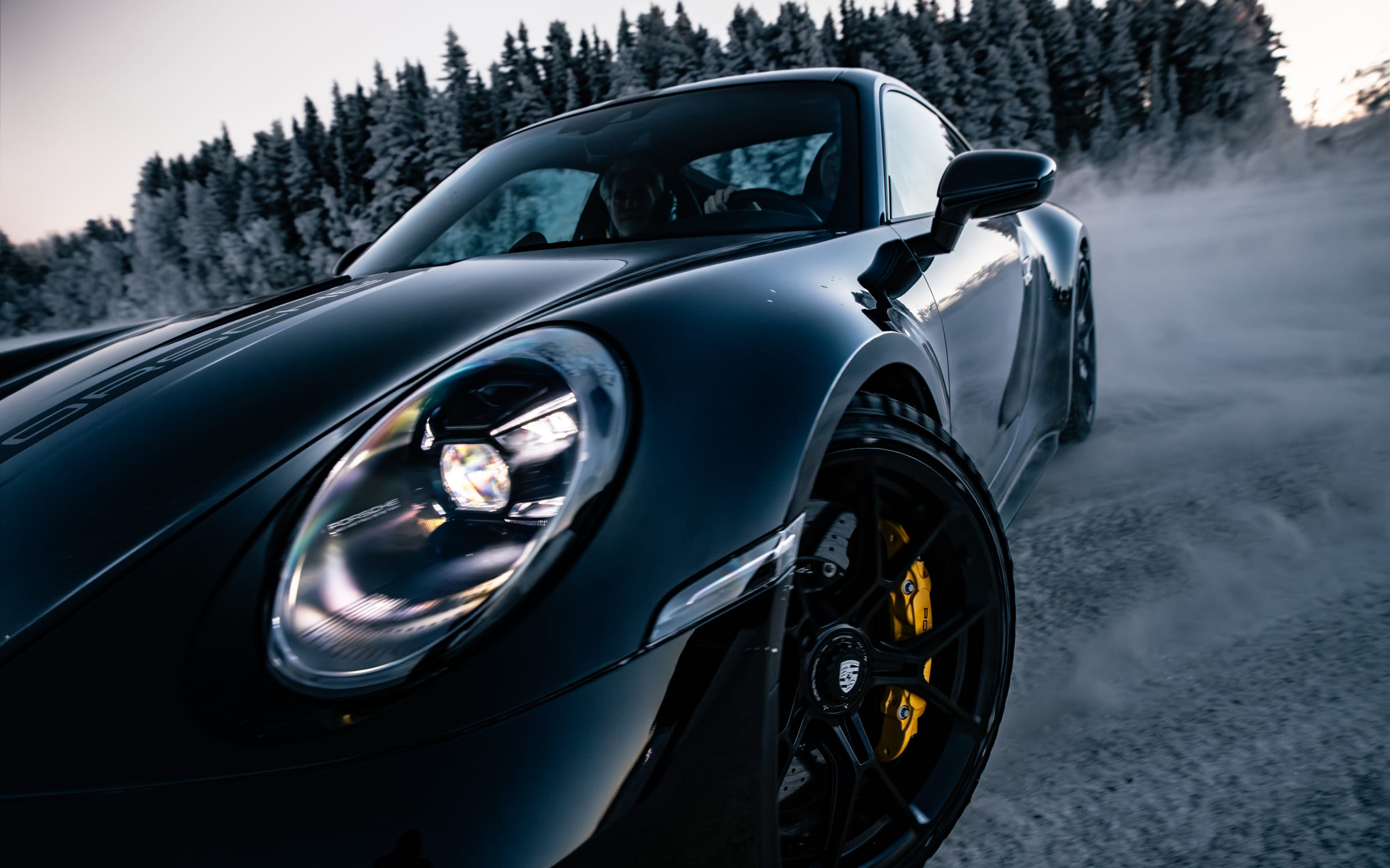 Zbliżenie przodu czarnego Porsche 911 na tle ośnieżonego lasu