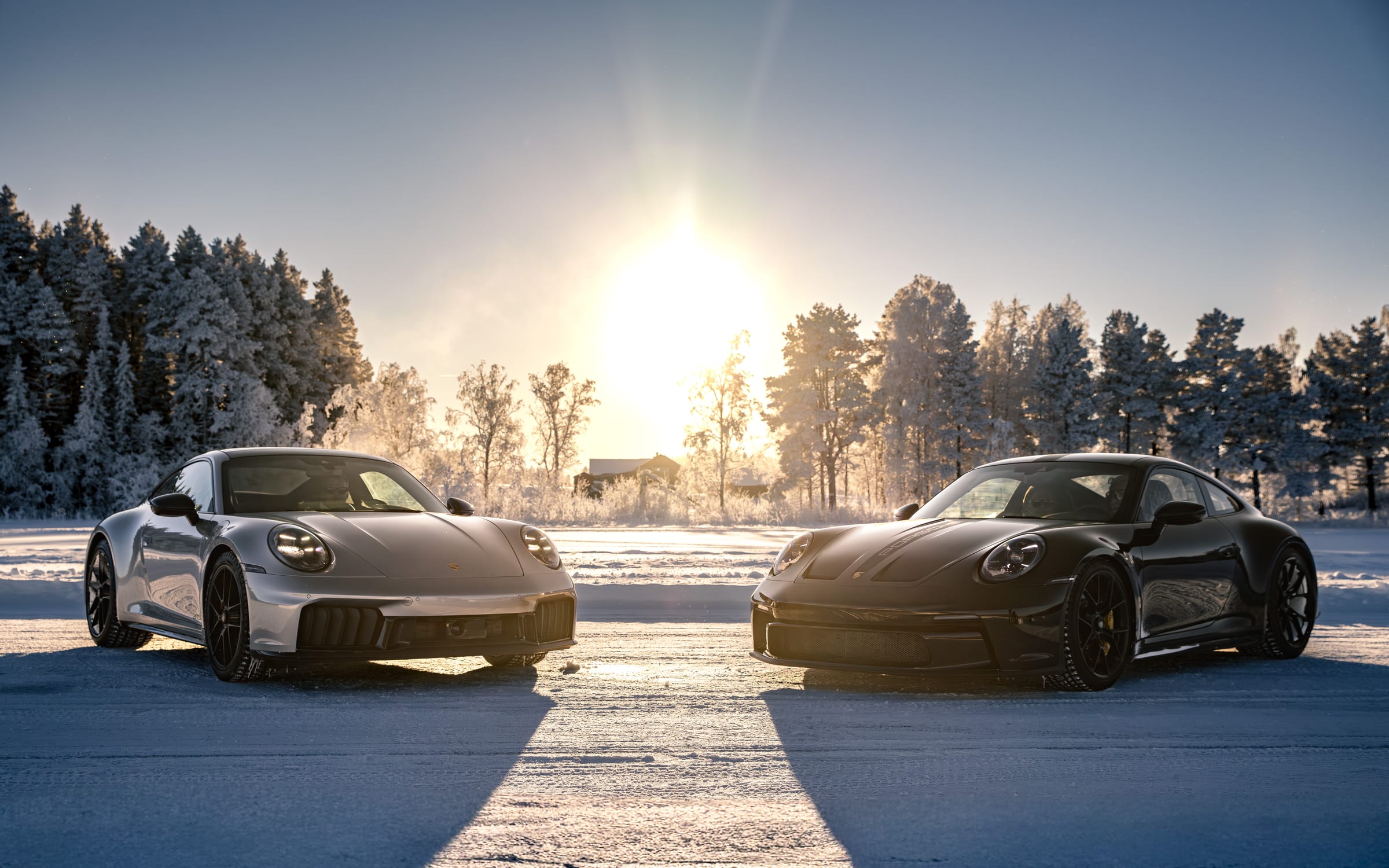 Dwa Porsche 911 naprzeciw siebie na zamarzniętym jeziorze pod niskim zimowym słońcem